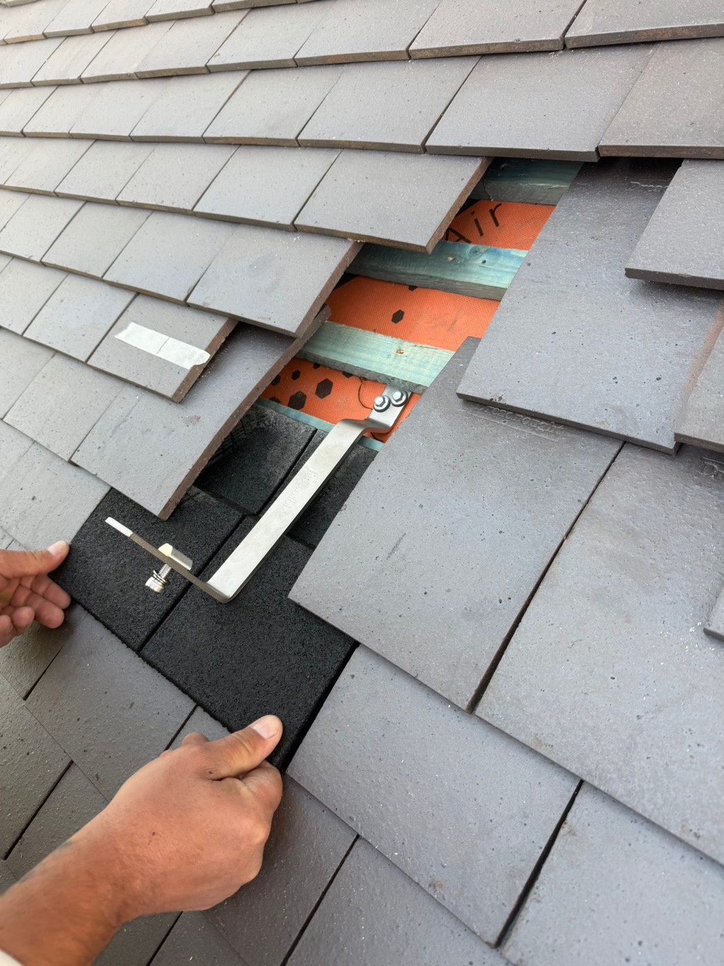 Installer fitting a stainless-steel roof anchor beneath the tiles by hand